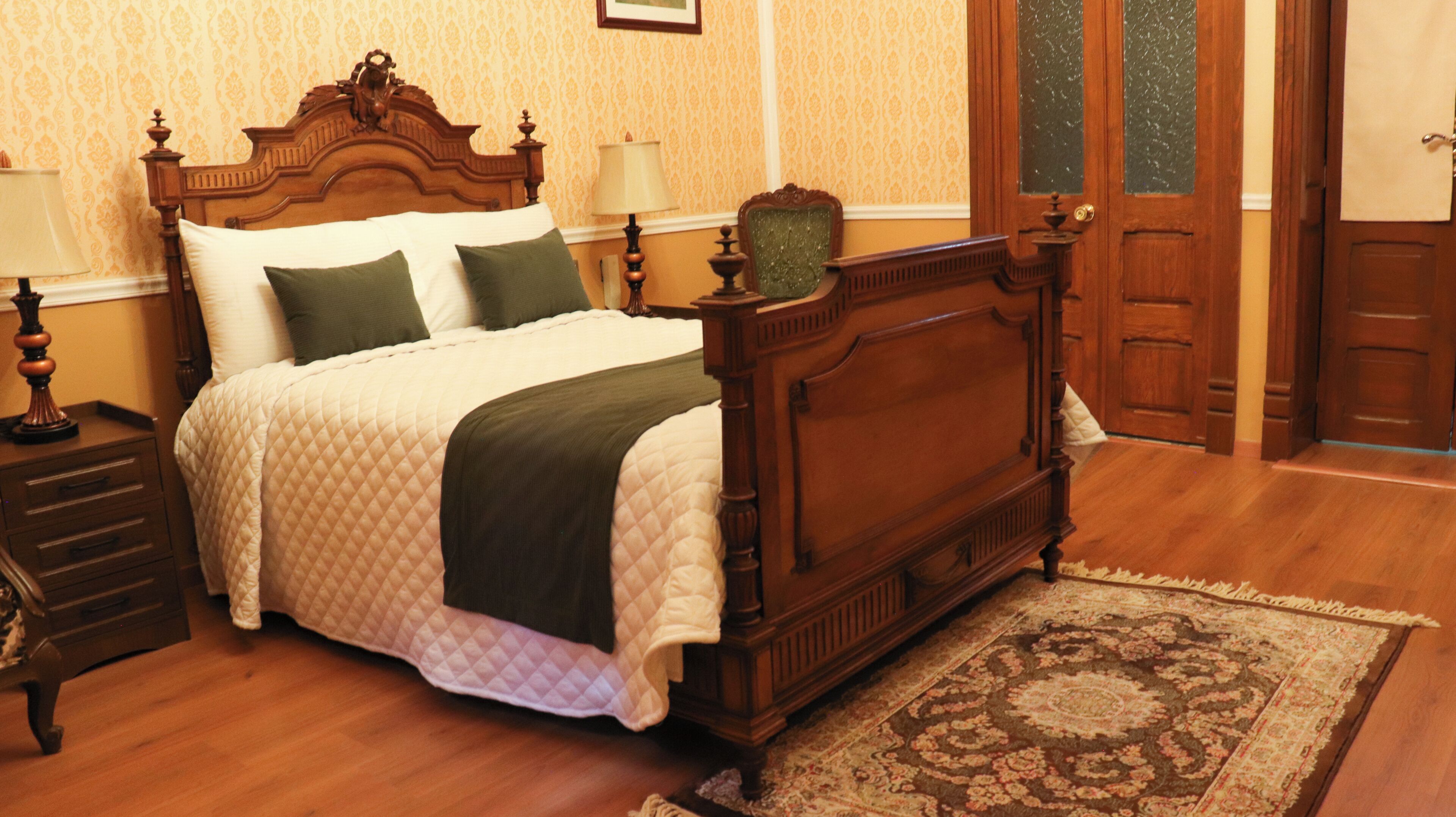 A traditional bedroom with a wooden bed, a nightstand, a lamp, and a patterned rug.