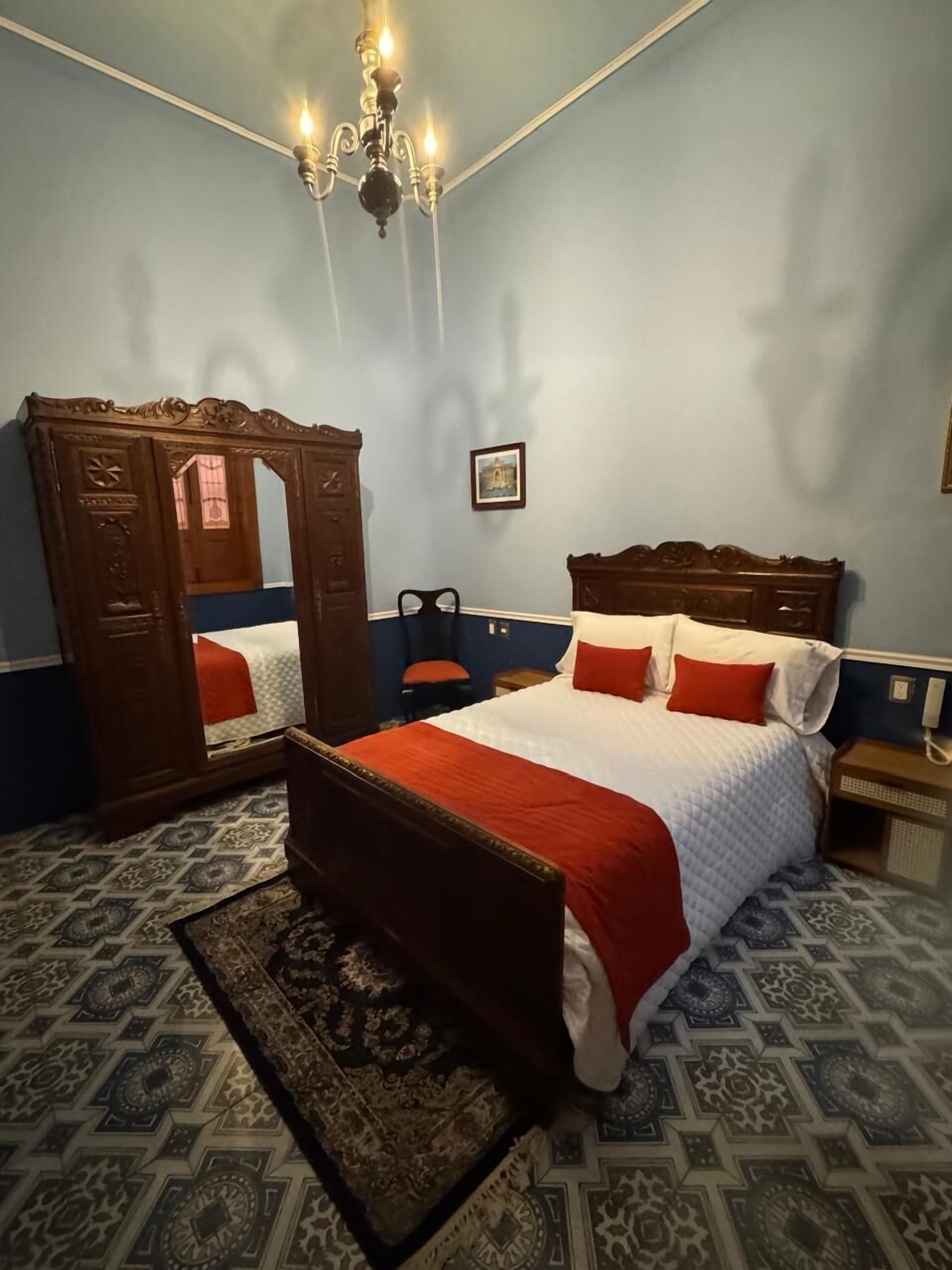 A bedroom with a large bed, a wooden wardrobe, a mirror, and a chandelier.