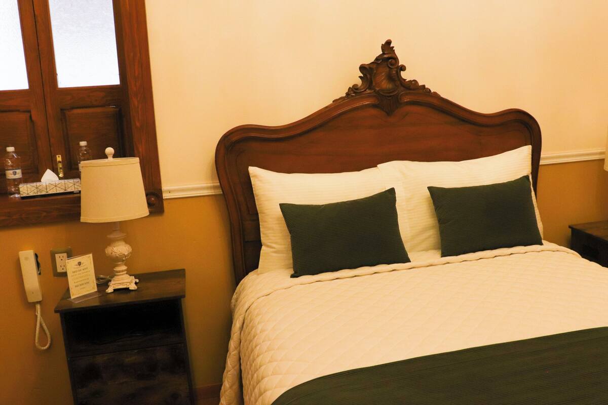 A neatly made bed with a wooden headboard, two bedside tables with lamps, and a wall socket.