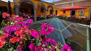 A courtyard with vibrant flowers, yellow walls, and a red umbrella.