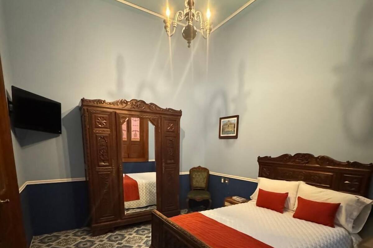 A bedroom with a four-poster bed, a large mirror, a chandelier, and patterned carpet.