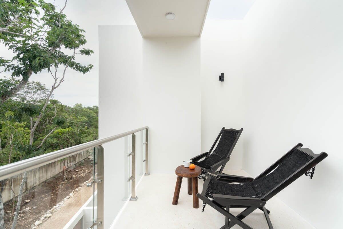 Un balcon avec deux fauteuils noirs, une petite table en bois et une balustrade blanche.
