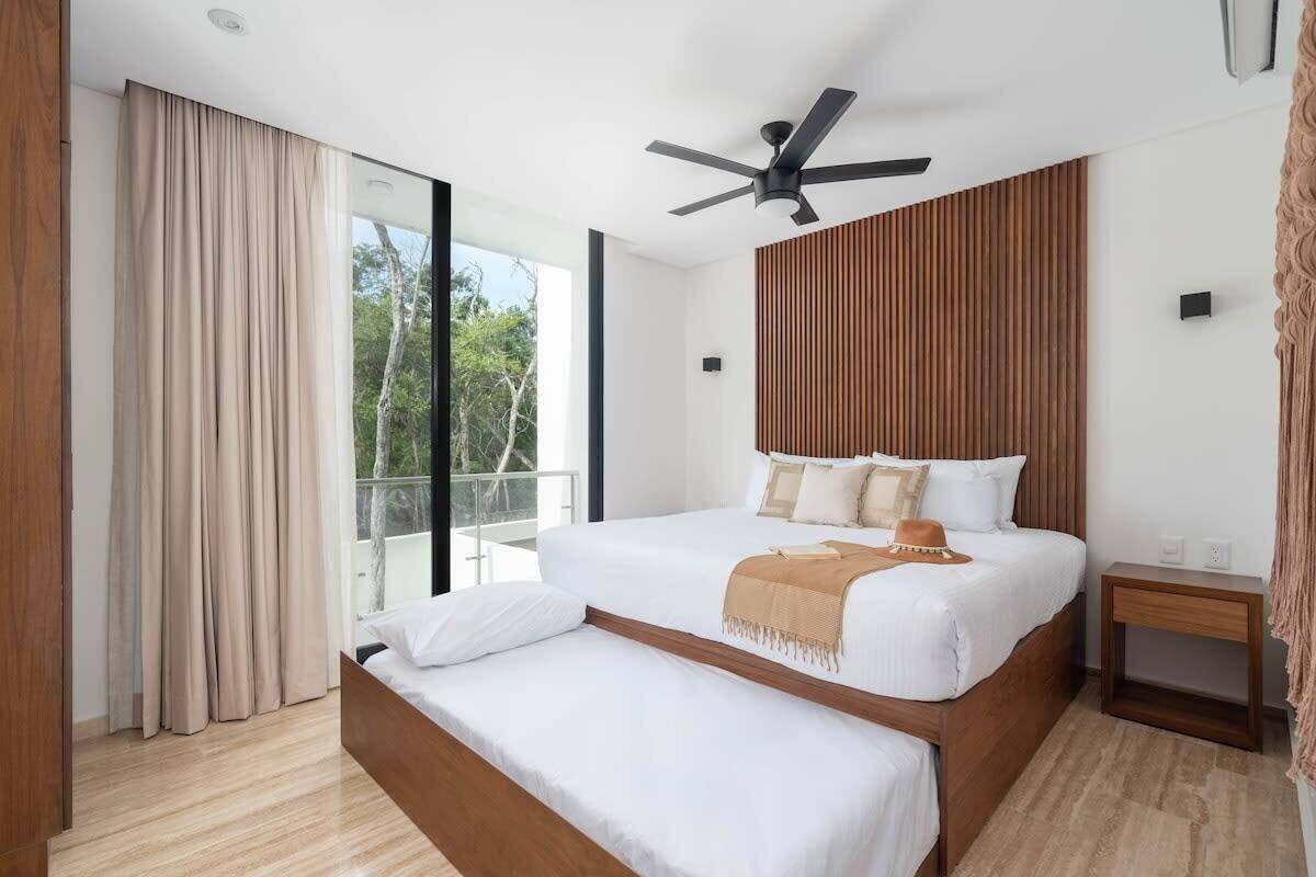 A modern bedroom with a large bed, a ceiling fan, and a view of the outdoors.