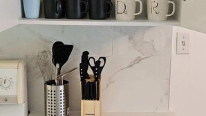 Eine Küche mit weißer Arbeitsplatte, einem Schubladeneinsatz für Küchenutensilien und einem Regal mit Gläsern und Tassen.