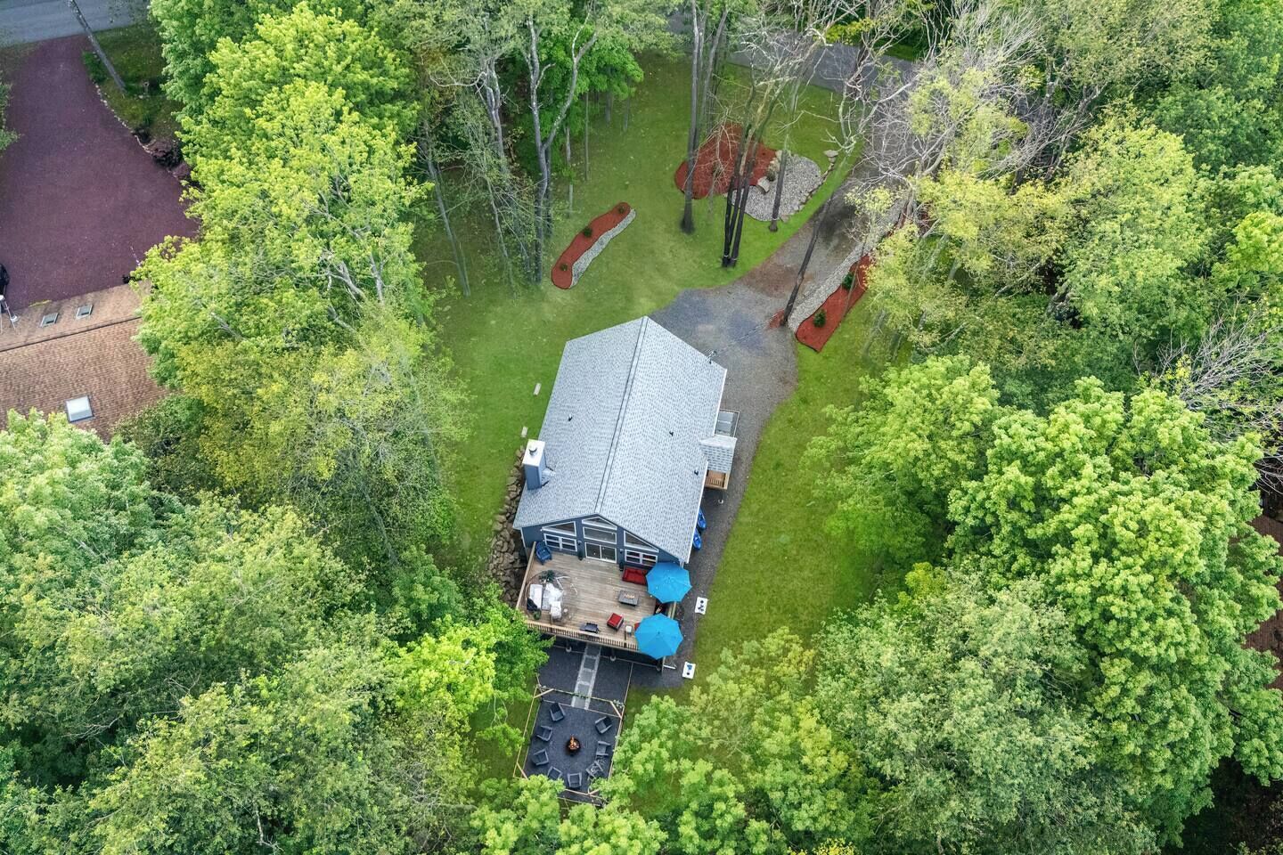 Luftaufnahme eines Hauses, umgeben von dichten Bäumen, mit einer Terrasse und Sitzgelegenheiten im Freien.