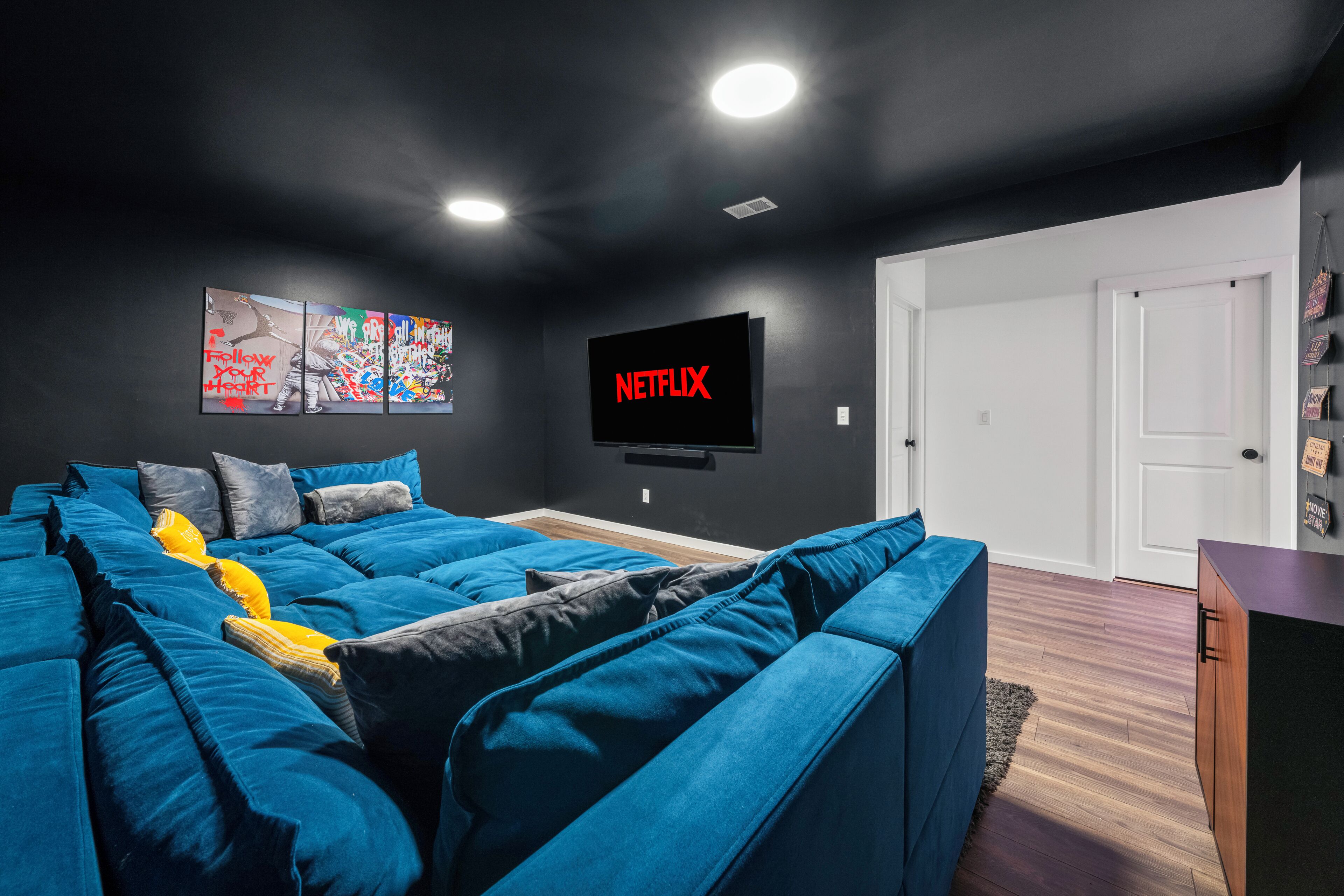 A modern living room with a sectional sofa, a flat-screen TV mounted on the wall, and a door leading to another room.