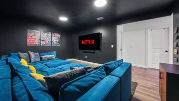 A modern living room with a sectional sofa, a flat-screen TV mounted on the wall, and a door leading to another room.