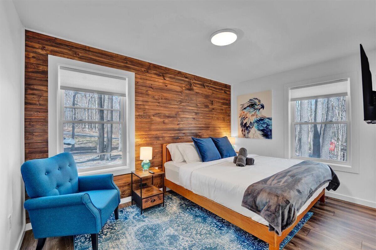 Ein Schlafzimmer mit einer Wand aus Holzpaneelen, einem großen Bett, einem blauen Sessel und einem Gemälde eines Vogels.