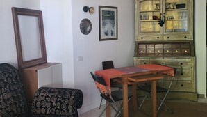 Un soggiorno con un tavolo da pranzo, due poltrone fantasia, un mobiletto con vetrine e un quadro incorniciato appeso al muro.