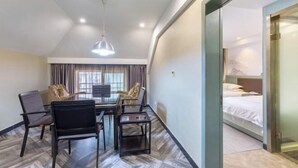 A hotel room with a bed, a desk with chairs, a large window with curtains, and a hanging light fixture. - Jinteng Hotel (Yiwu)