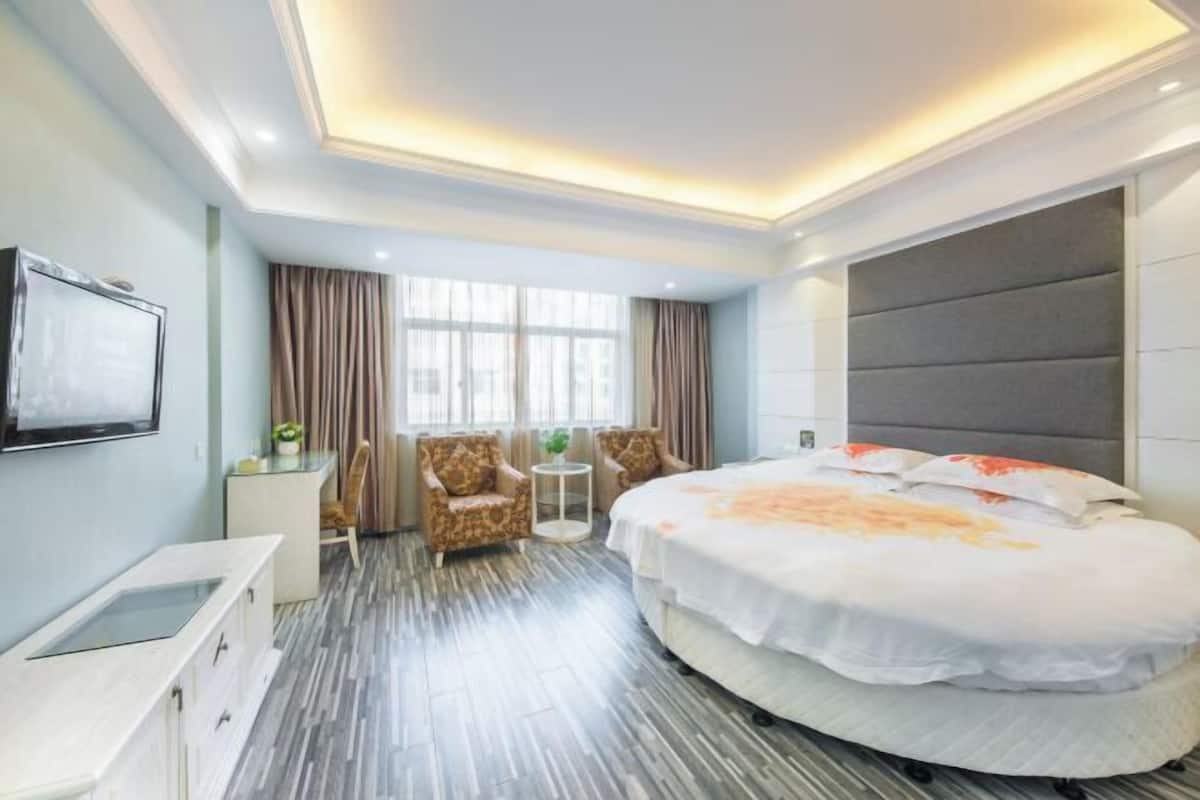 A hotel room with a bed, two armchairs, a small table, and a TV.