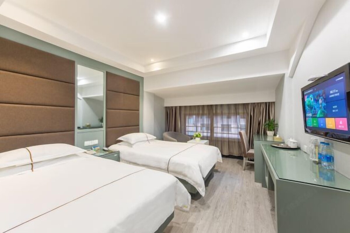 Habitación de hotel con dos camas, televisión, escritorio, silla y ventana con cortinas.