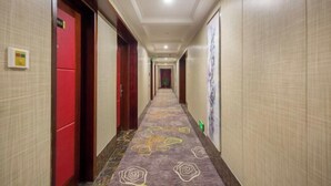 A hotel hallway with a patterned carpet, red doors, and a long corridor. - Jinteng Hotel (Yiwu)