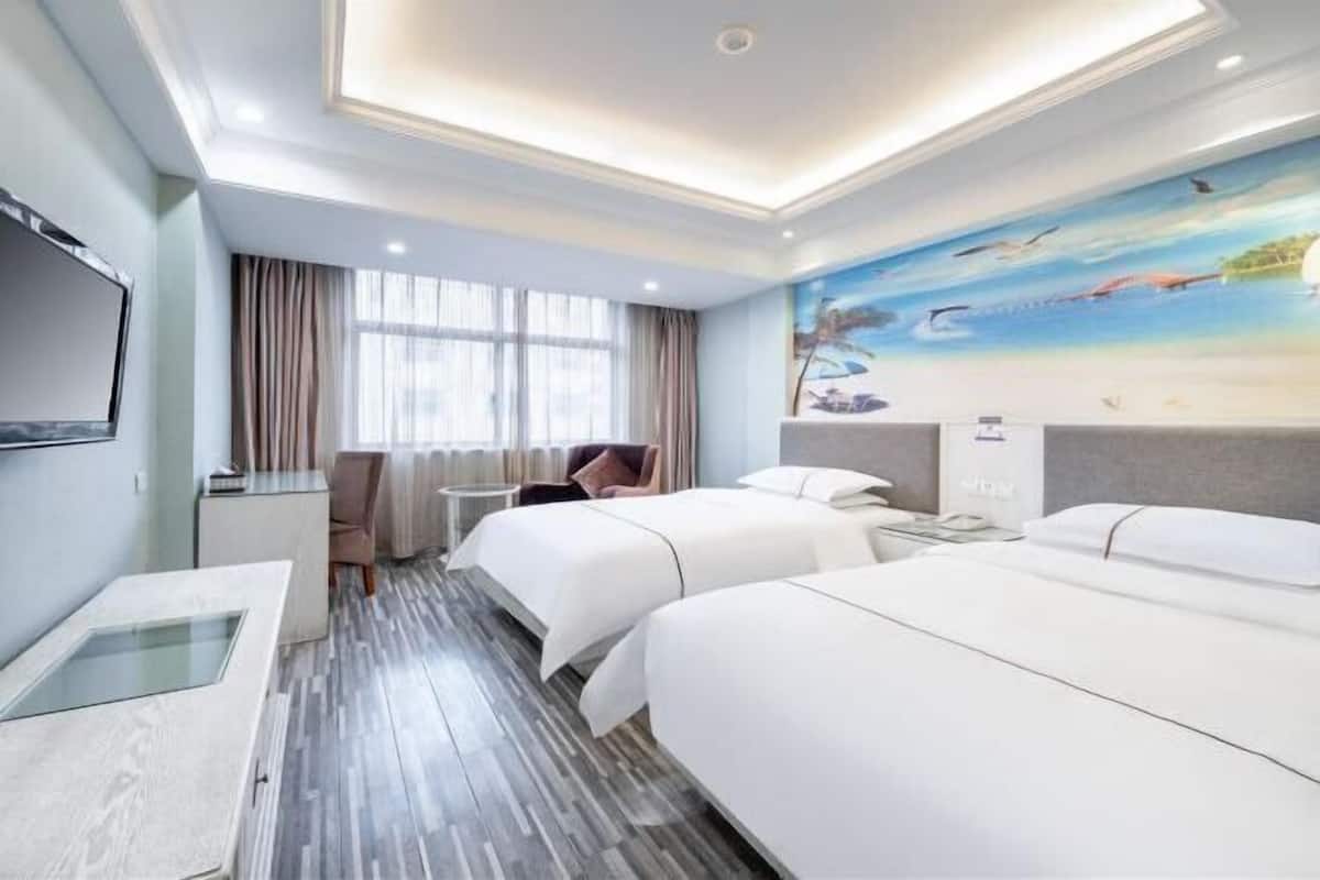 A hotel room with two beds, a desk, a TV, and a mural of a beach scene.