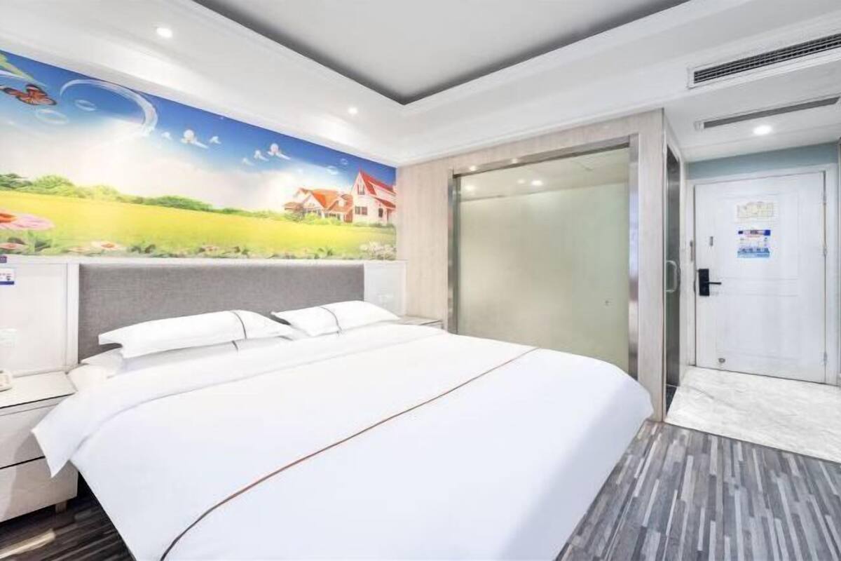 A modern hotel room with a large bed, a mural on the wall, a sliding door, and a small desk with a chair.