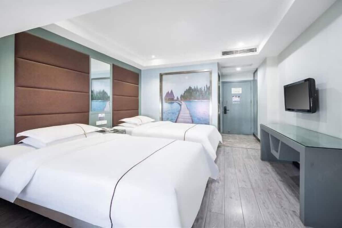 A hotel room with two beds, a flat-screen TV, a painting, and a view of a body of water.
