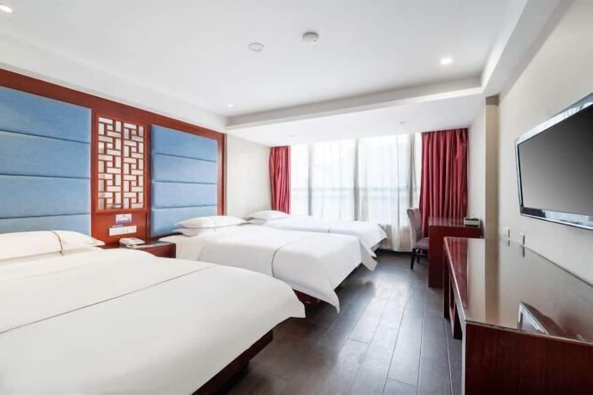 A hotel room with three beds, a TV, and a large window with curtains.