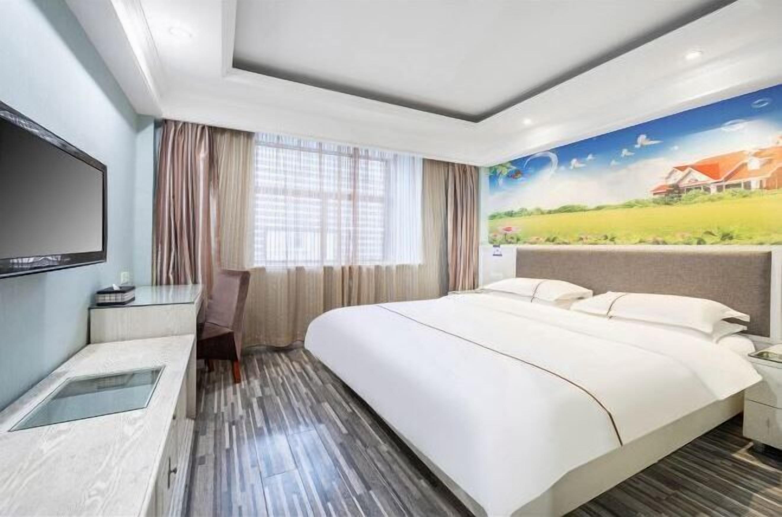 A hotel room with a large bed, a desk, a chair, a TV, and a mural on the wall.