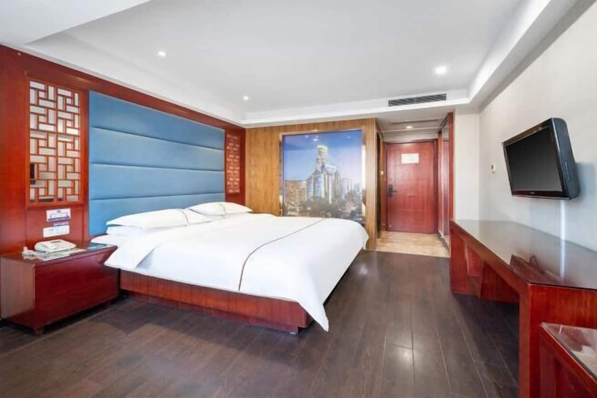 A hotel room with a large bed, a TV, a wooden nightstand, and a wall-mounted TV.