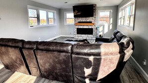 Een moderne woonkamer met een grote leren hoekbank, een open haard en een flatscreen televisie aan de wand.