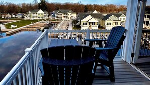 Een terras met twee Adirondack-stoelen met uitzicht op een jachthaven met boten en huizen op de achtergrond.