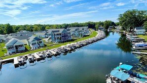 Een jachthaven met aangemeerde boten, een rij huizen langs het water, en een heldere lucht.