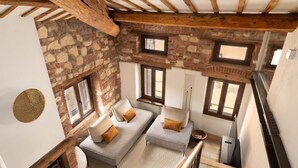 A loft-style room with exposed brick walls, a stone fireplace, and a wooden ceiling. There are two grey sofas with cushions, a round rug, and a staircase leading to an upper level. - River Cross ✔ Self Check-In (Verona)