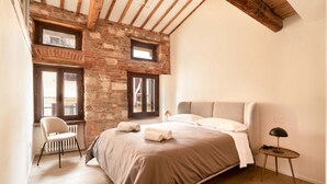 A bedroom with a bed, a chair, a lamp, and a brick wall. - River Cross ✔ Self Check-In (Verona)
