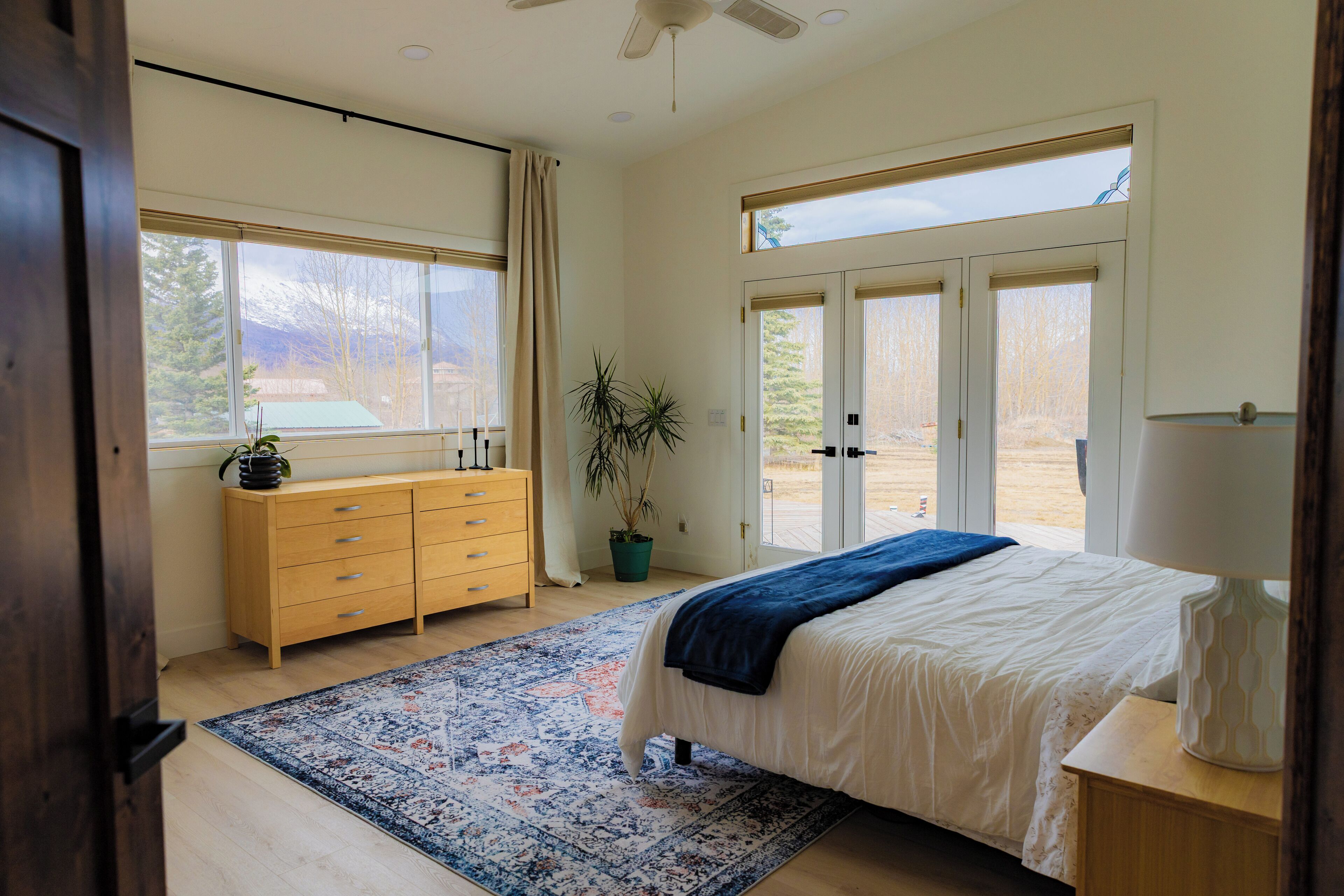 A bedroom with a bed, a dresser, a potted plant, and a view of the outdoors.