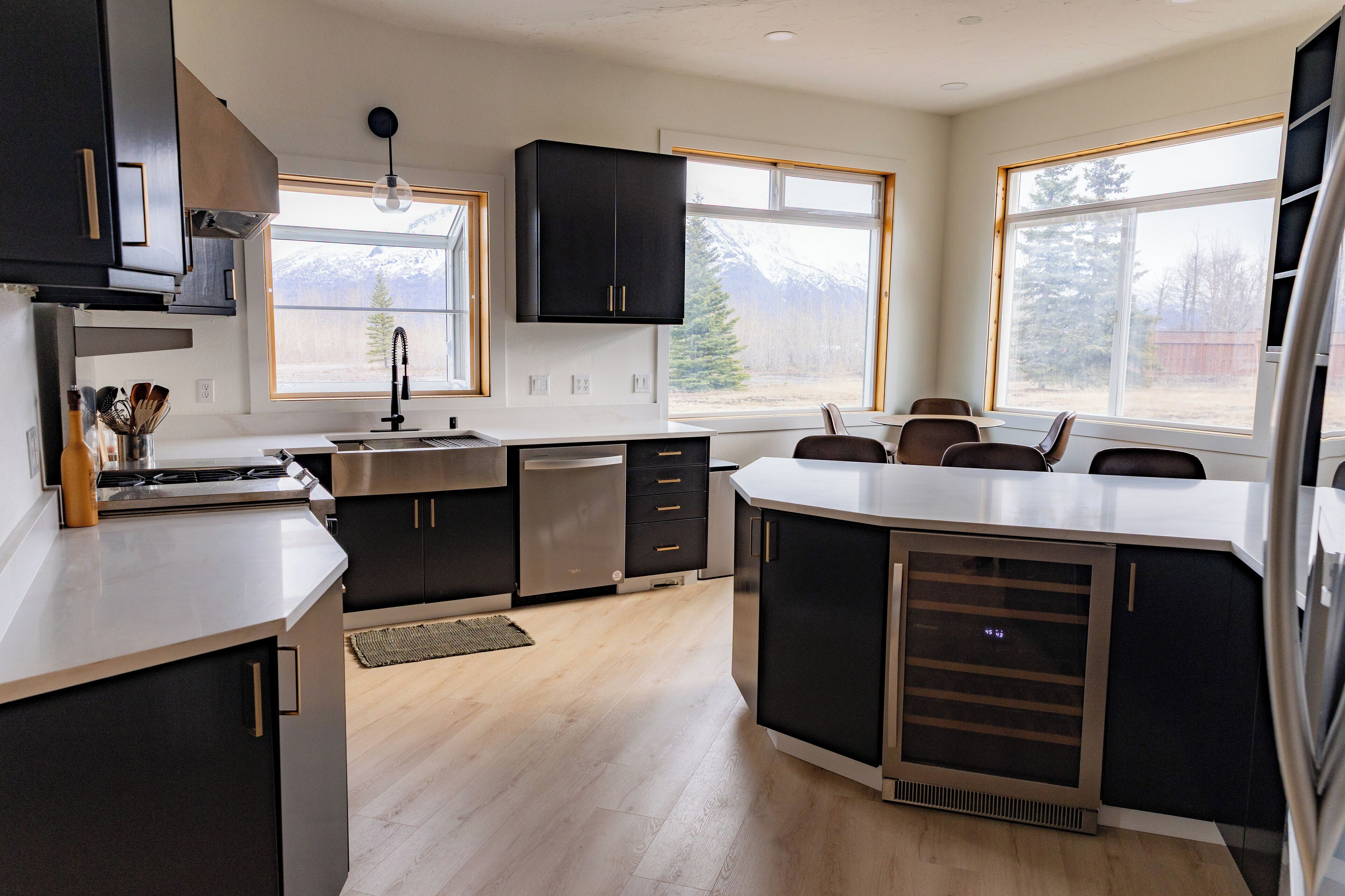 A modern kitchen with a central island, stainless steel appliances, and large windows offering views of mountains.