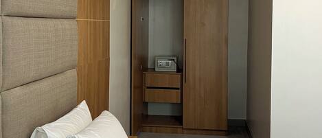 A hotel room with a bed, a large padded headboard, a wooden wardrobe, and a small bedside table with a radio.