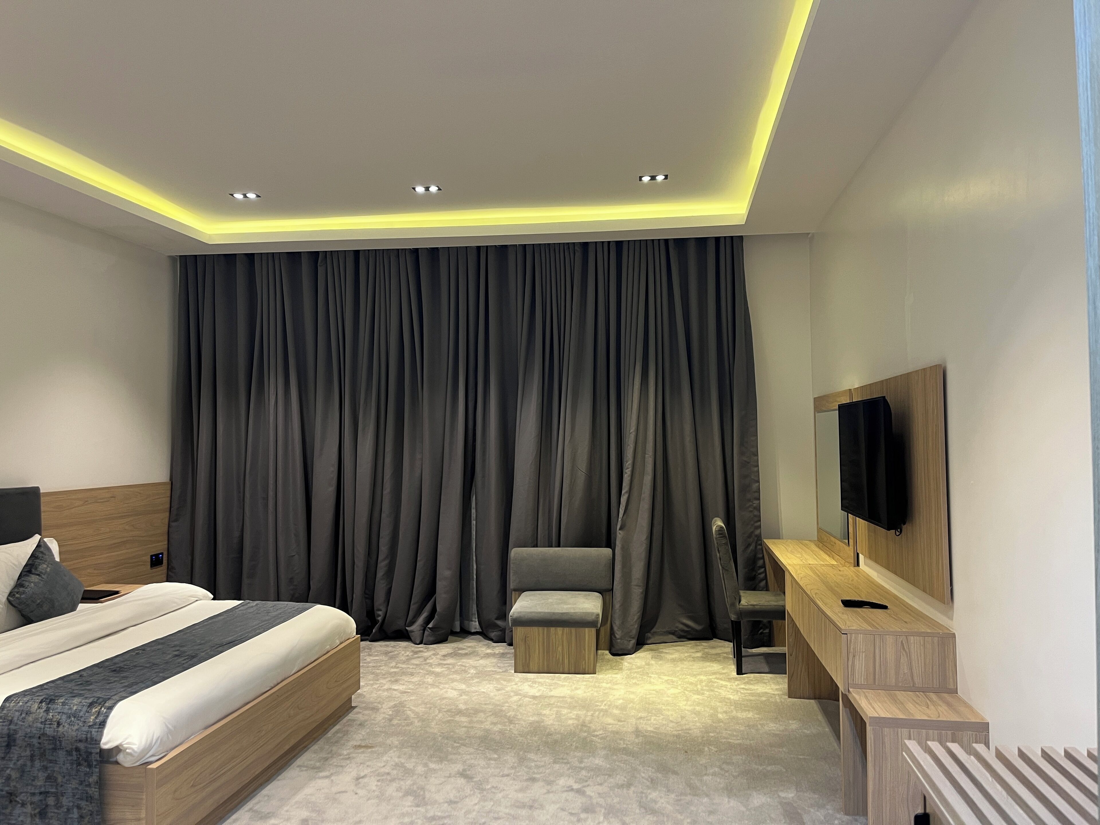 A modern hotel room with a large bed, a desk, a chair, and a TV mounted on the wall.