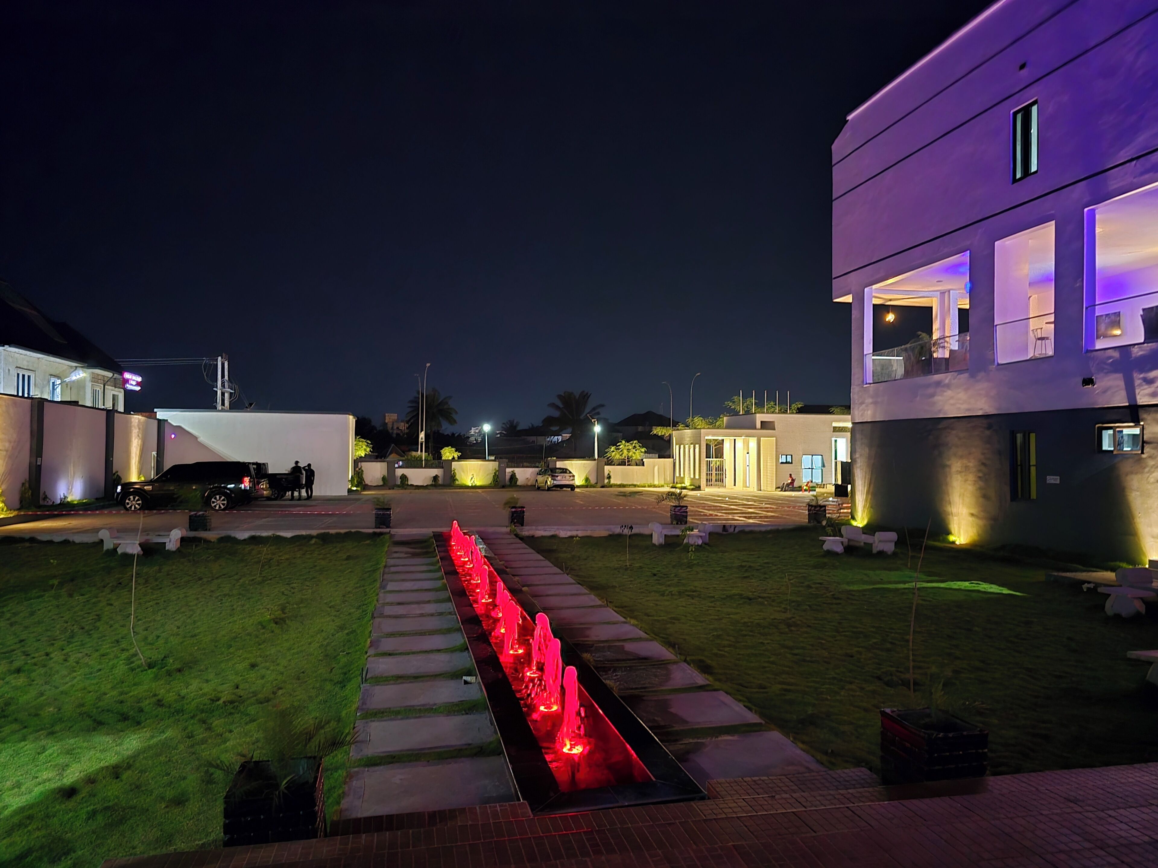 A modern building with a well-lit entrance, a pathway leading to the main entrance, and a landscaped garden area.