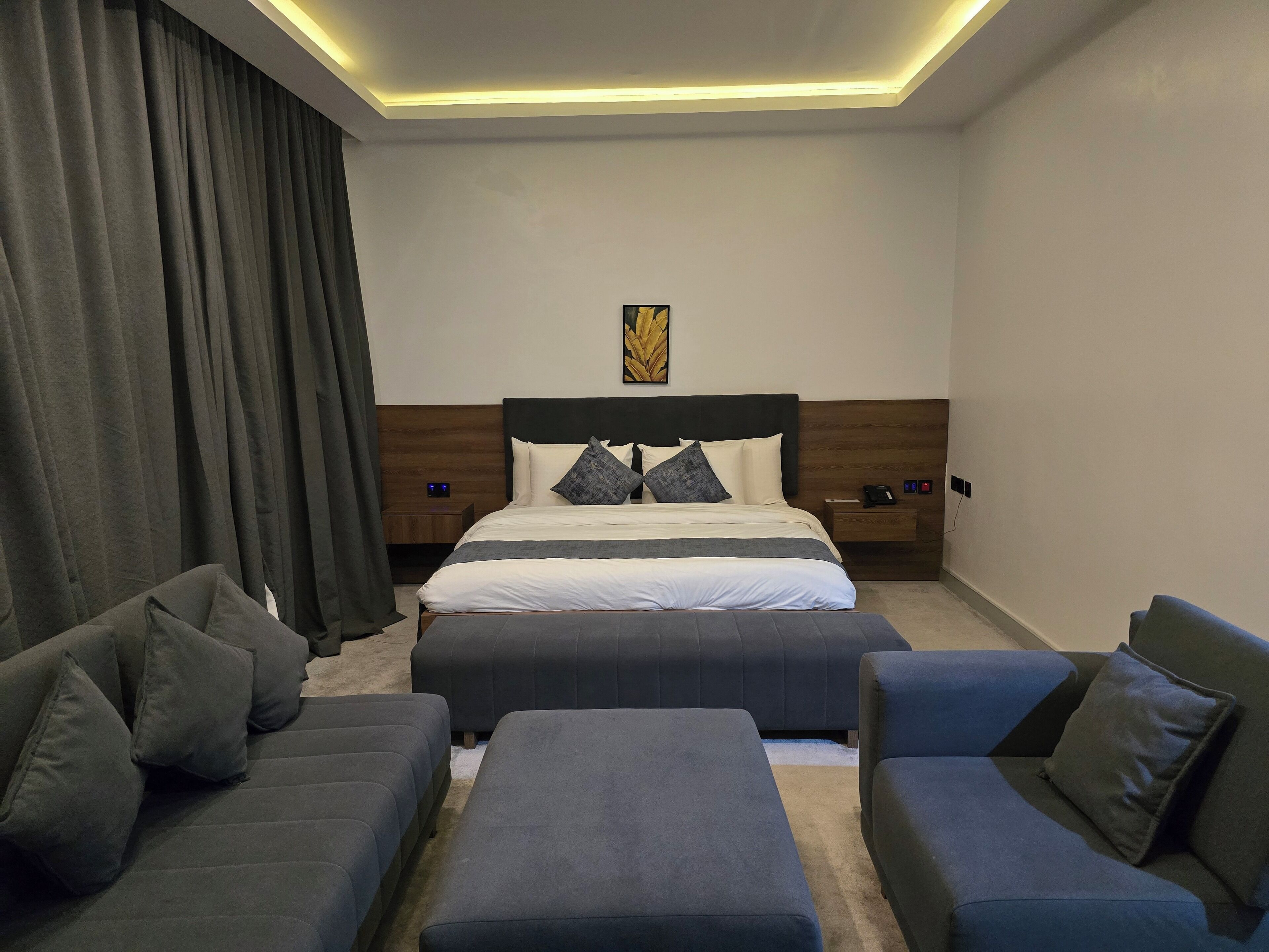 Una habitación de hotel moderna con una cama grande, dos sofás, una mesita de centro y una mesita de noche con un teléfono y una lámpara.