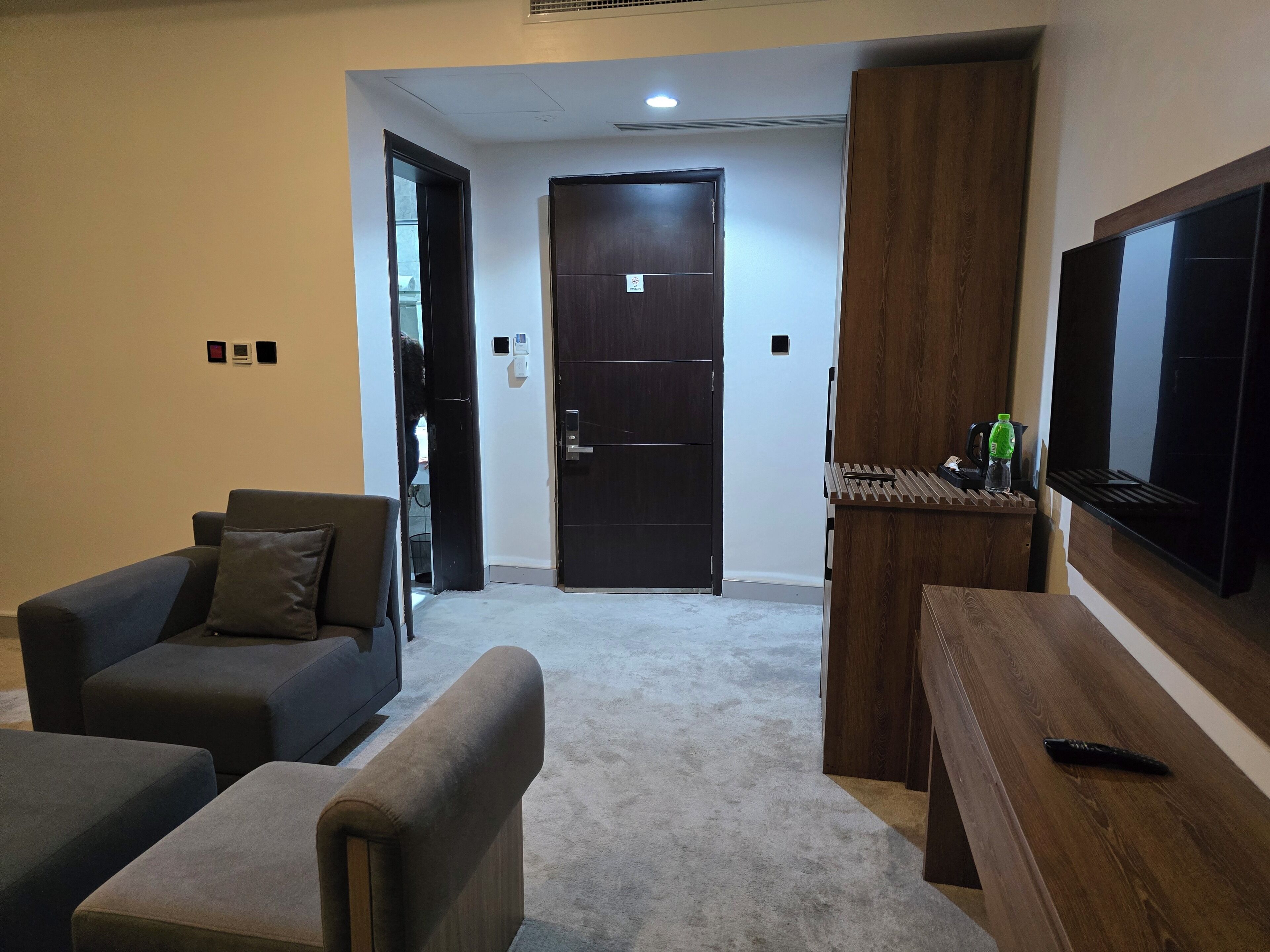 Una sala de estar con un sofá, un reposapiés y una mesa de centro de madera. Se observa una puerta al fondo que da a otra habitación.