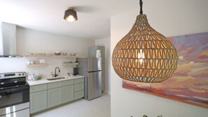 Uma cozinha moderna com luminária pendente trançada, eletrodomésticos de aço inoxidável e um quadro abstrato colorido na parede.