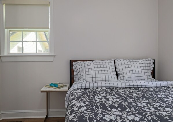 Une chambre à coucher avec un lit, une petite table de chevet, une fenêtre et une vue sur l’extérieur.