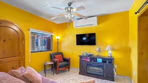 A living room with a ceiling fan, a TV mounted on the wall, a sofa, a chair, and a small table.
