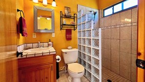 A bathroom with a wooden vanity, a toilet, a glass shower enclosure, and a mirror with lights.
