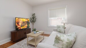 Una sala de estar con televisor de pantalla plana, un mueble de madera, una mesa de centro, un sofá y una ventana con persianas.
