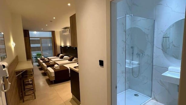 A hotel room with a glass-enclosed shower, a sitting area with a sofa and a table, and a view of the outside. - Purple 4: Studio Apartment in St. Julian's (Swieqi)
