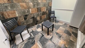 Um espaço exterior pequeno e fechado, com um muro de pedra, duas cadeiras e uma mesa.