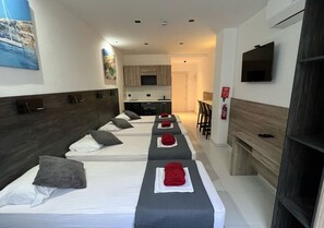 Habitación de hotel con tres camas, televisión y kitchenette.