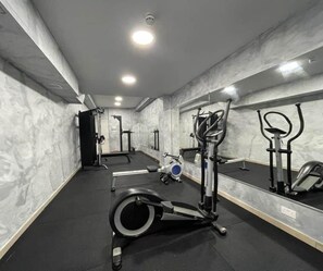 A gym with exercise equipment, a mirror, and a door in the background. - Orange 8: Studio Apartment in St. Julian's (Swieqi)