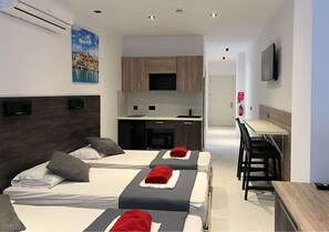A hotel room with three beds, a kitchenette, a dining area, and a TV mounted on the wall. - Purple 5: Studio Apartment in St. Julian's (Swieqi)