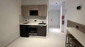 A compact kitchen with a microwave, sink, and wooden cabinets. - Purple 9: Studio Apartment in St. Julian's (Swieqi)