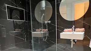 A modern bathroom with a glass-enclosed shower, a round mirror, and a white sink with a towel. - Purple 9: Studio Apartment in St. Julian's (Swieqi)