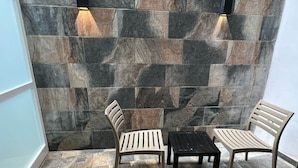 A corner with two wooden chairs and a small table, set against a wall with large, multicolored stone tiles. - Purple 9: Studio Apartment in St. Julian's (Swieqi)
