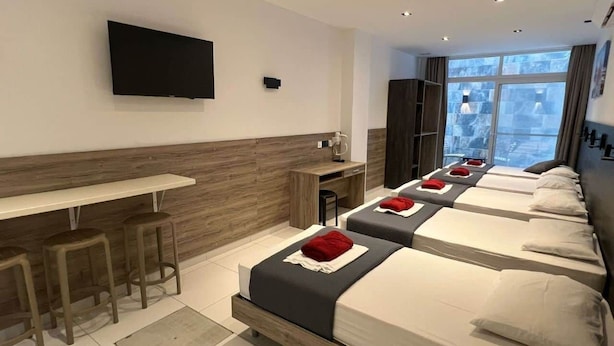 A hotel room with a long bed, a desk, and a TV. - Purple 9: Studio Apartment in St. Julian's (Swieqi)