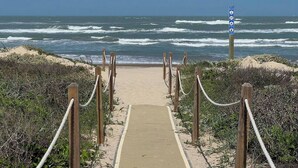 Uma trilha de praia que leva ao oceano, com uma placa visível.